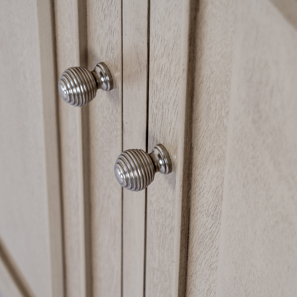 Close-up of the cabinet's two silver-coloured ribbed knobs beside raised door mouldings and the pale grey-beige grained finish.