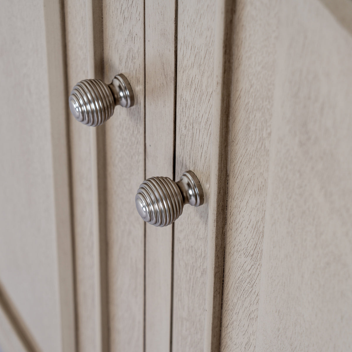 Close-up of the cabinet's two silver-coloured ribbed knobs beside raised door mouldings and the pale grey-beige grained finish.