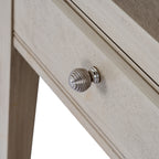 Close-up of the round silver-coloured drawer knob with concentric ribs against the pale grained drawer front.