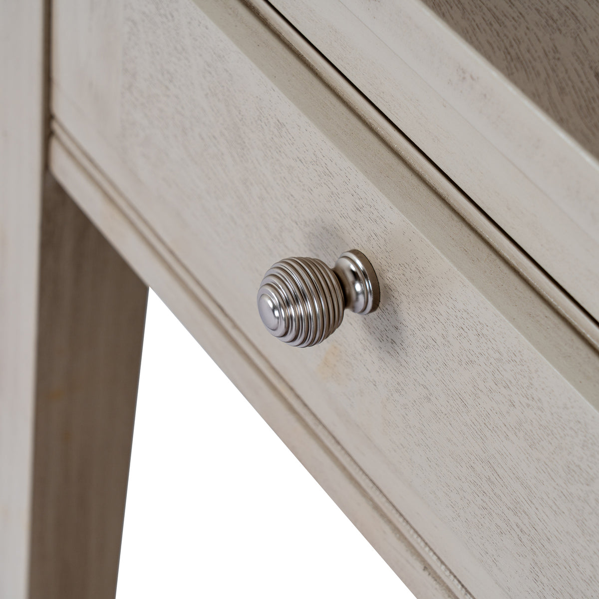 Close-up of the round silver-coloured drawer knob with concentric ribs against the pale grained drawer front.