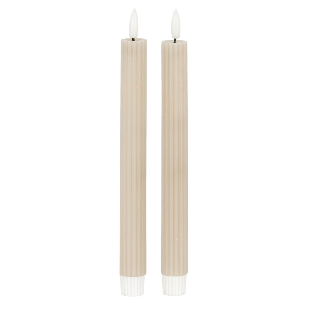Two slender pale beige-taupe ribbed candles with white flame-shaped tips and white lower fittings against a white background.