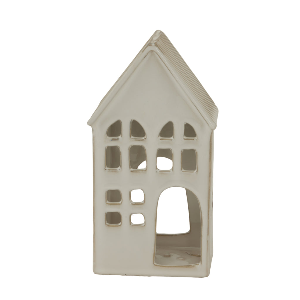 Near-front view of the cream-white house candle holder, showing rows of irregular windows and a large arched doorway on the right.