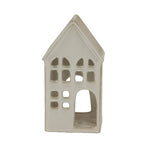 Near-front view of the cream-white house candle holder, showing rows of irregular windows and a large arched doorway on the right.