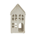 Front view of a cream-white house-shaped candle holder with a steep pitched roof, rows of window cut-outs and a large arched doorway.