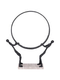 Front view of two black abstract figures holding a large circular ring on a pale rectangular marble base.