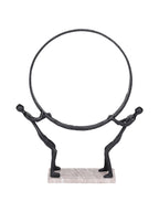 Front view of two black abstract figures holding a large circular ring on a pale rectangular marble base.