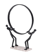 Angled view of the ring-bearing figures sculpture, showing the depth of the black ring and rectangular marble base.