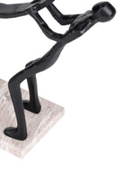 Detail of a leaning black figure with bent legs and raised arms, standing on the pale veined marble base.