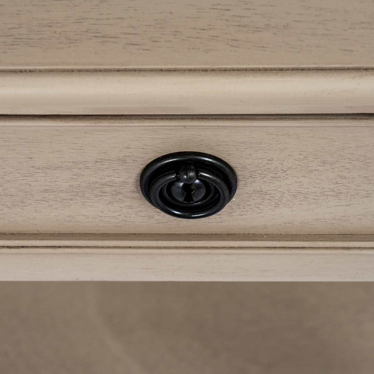 Close-up of a black ring pull centred on a pale grained drawer front with a raised rectangular border.