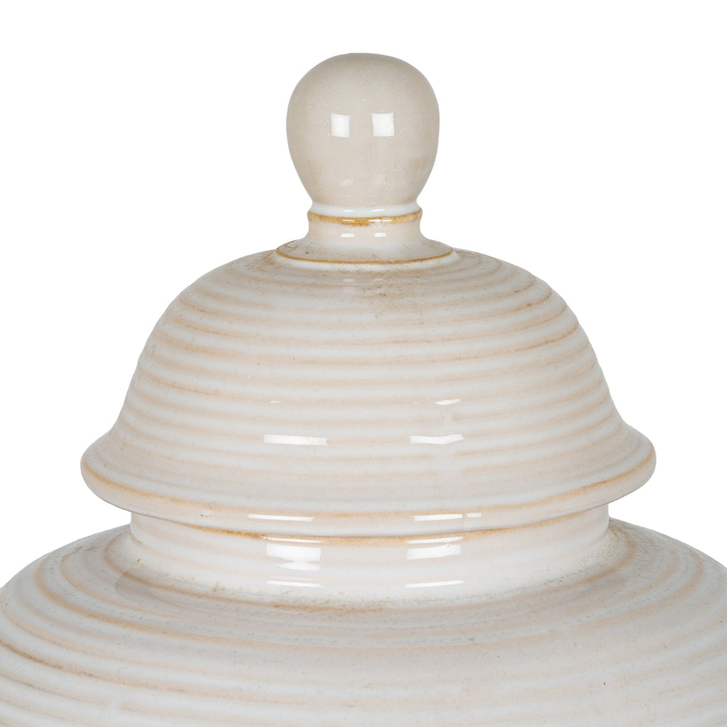 Close-up of the jar's rounded finial and ribbed domed lid, showing glossy cream-white surfaces and warm beige accents.