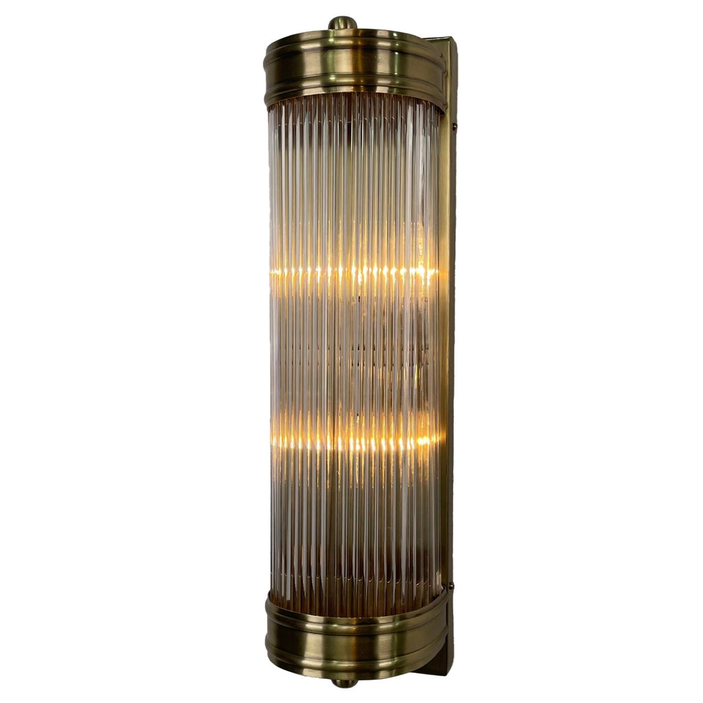 Illuminated Rod Shade Wall Light at a slight angle, with vertical glass rods, antique-brass-finished end bands and a rectangular backplate.