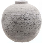 Rounded grey-beige vase with a short open neck, rough surface and irregular dark speckles and horizontal bands against a white background.