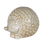 Cream-white hedgehog decoration facing left, showing its blunt nose, curled ear, short feet and glossy overlapping scales with brown shading.