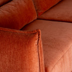 View over a rounded sofa arm highlighting the raised edge seam, with rust-orange seat and back cushions behind.
