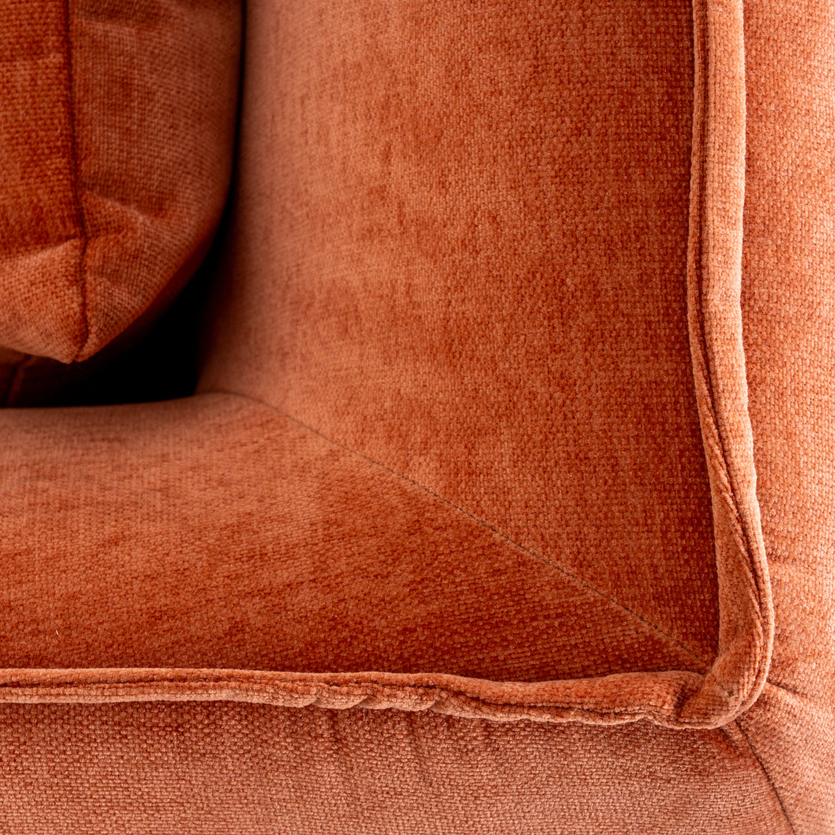 Close-up of the rust-orange upholstery inside the armchair, showing its surface texture and raised edging beside the seat cushion.