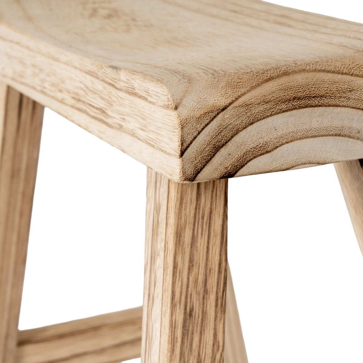 Close-up of the stool seat corner showing curved dark grain markings, the shallow dip in the top and streaked legs below.