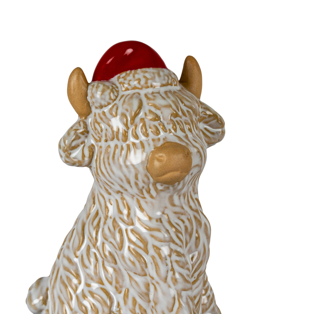 Close-up of the cow figure's glossy red Santa hat, pale textured trim, tan horns and rounded muzzle beneath a raised cream-and-tan shaggy fringe.