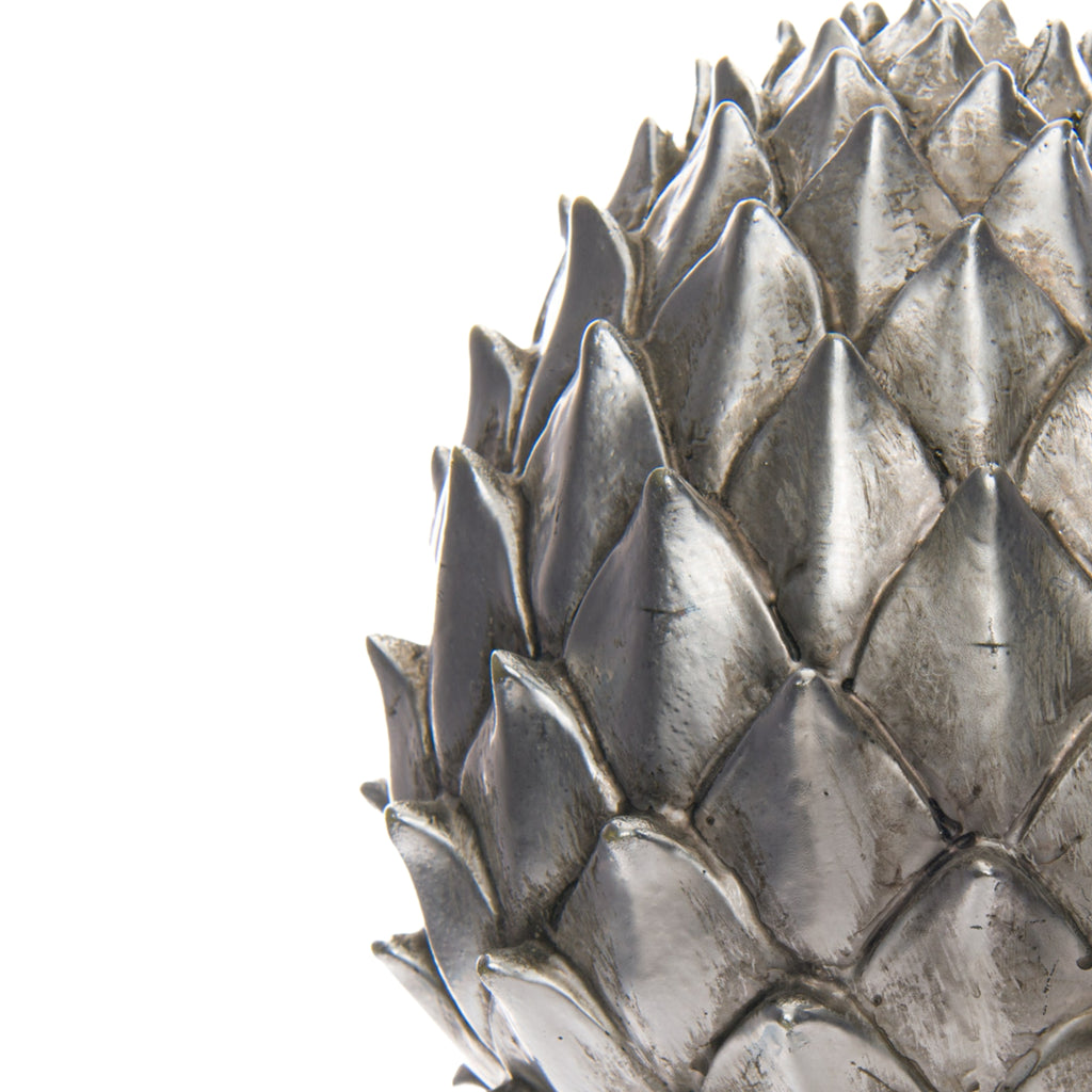 Close-up of the pinecone finial's overlapping scales, showing bright silver-coloured ridges, darker recesses and mottled surface markings.