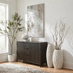 Pale ribbed vases beside a dark fluted cabinet, with tall twisting branches in the front vase and framed artwork above.