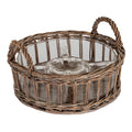 Round brown woven carrier with two arched loop handles, shown at an angle holding an empty transparent dish with a circular centre well and shaped surrounding sections.
