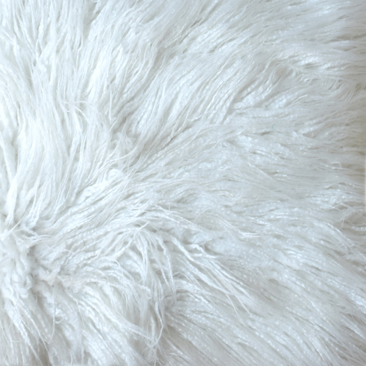 Close-up of the pouffe's ivory shaggy surface, with long strands lying in different directions.