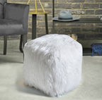Ivory shaggy cube pouffe on a pale floor beside a grey armchair, with a metal side table and exposed brick wall behind.