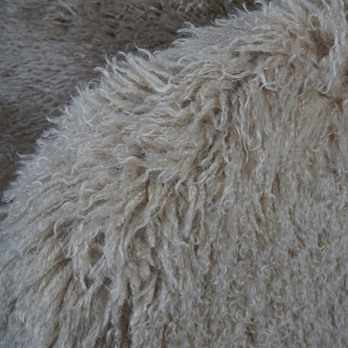 Close-up of long, loosely curled beige imitation-fur upholstery over the armchair's rounded arm.