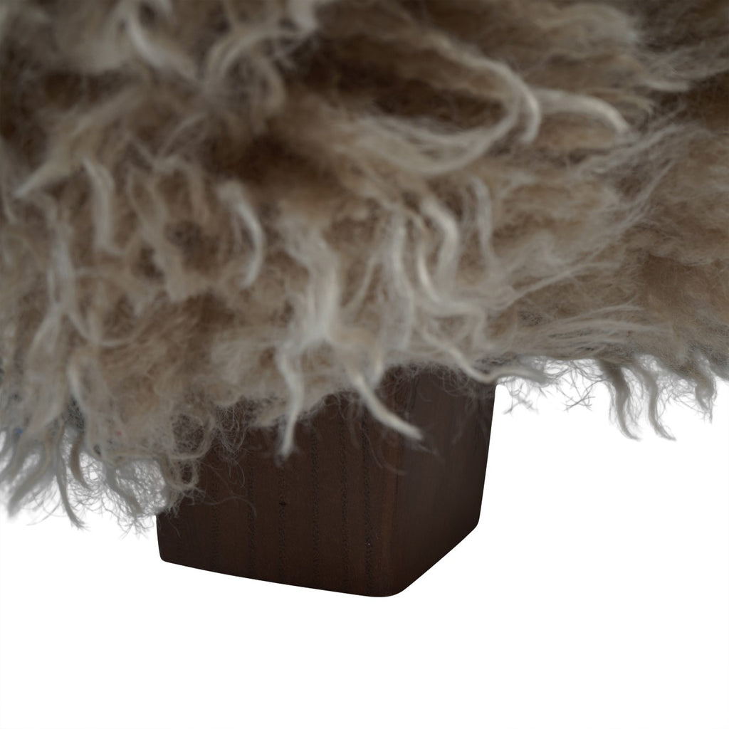 Close-up of a short dark wooden foot beneath the armchair's trailing beige shaggy upholstery.