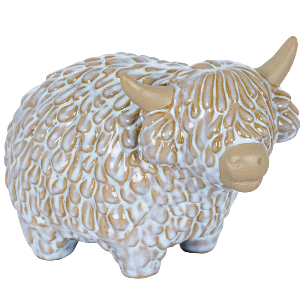 Three-quarter front view of a cream-and-white Highland cow ornament with curved horns, a shaggy fringe and short feet.