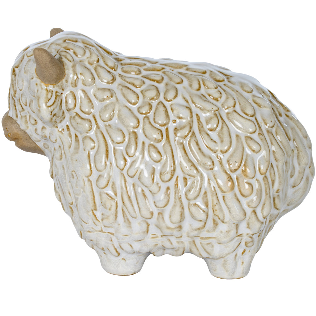 Side view of the Highland cow ornament facing left, showing the raised strands across its glossy white coat and rounded body.