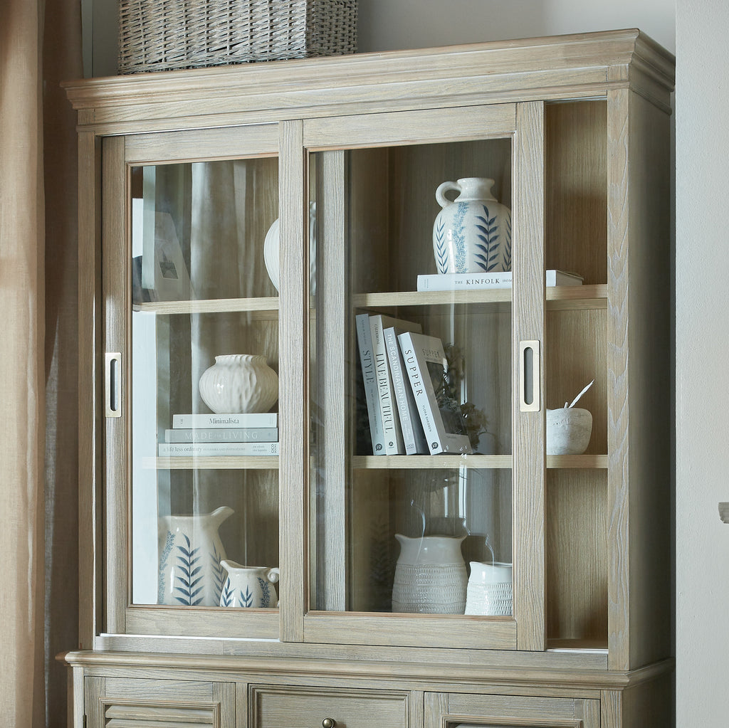 Upper dresser-top cabinet styled with books and white and blue-patterned ceramics, shown above an adjoining base unit beside a curtain.