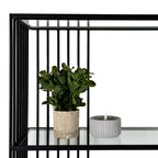 Close-up of a clear shelf beneath black vertical rods, styled with a leafy plant in a beige pot and a grey ribbed candle ornament.