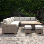 Pale woven-look corner seating with cream cushions, a rectangular slatted-top table and two square cushioned stools on patterned paving against dense greenery.