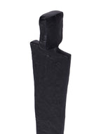Close-up of the sculpture's rectangular head and broad shoulders, showing the uneven texture of the black finish.