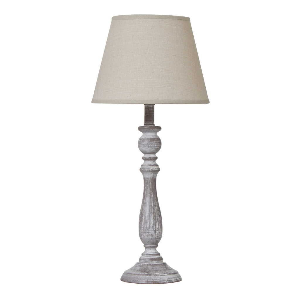 Table lamp with a tapered beige shade, slender whitewashed grey-brown column and round foot against a white background.