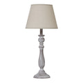 Table lamp with a tapered beige shade, slender whitewashed grey-brown column and round foot against a white background.