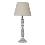 Table lamp with a tapered beige shade, slender whitewashed grey-brown column and round foot against a white background.