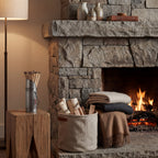 Silver match holder on a timber block beside a stone fireplace, with a basket of logs, folded blankets and a floor lamp.