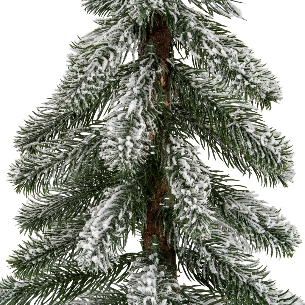 Close-up of drooping dark green pine-like needles with uneven white flocking around the textured brown trunk.