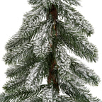 Close-up of drooping dark green pine-like needles with uneven white flocking around the textured brown trunk.