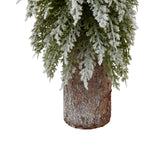 Close-up of the cylindrical bark-textured base beneath drooping green branches dusted with white snow-effect flocking.