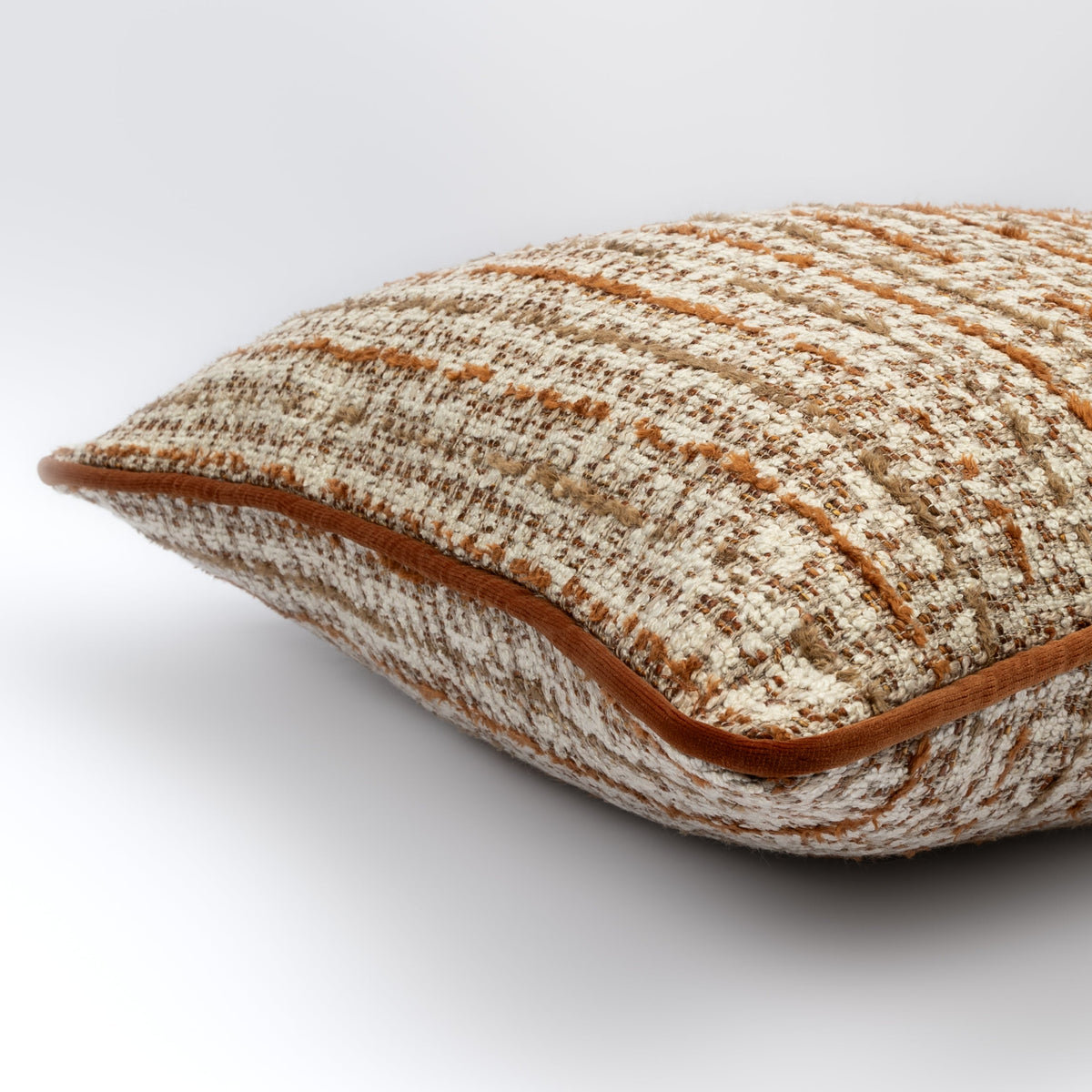 Angled view of the Solene Cushion showing its rust and cream woven pattern with rust piping