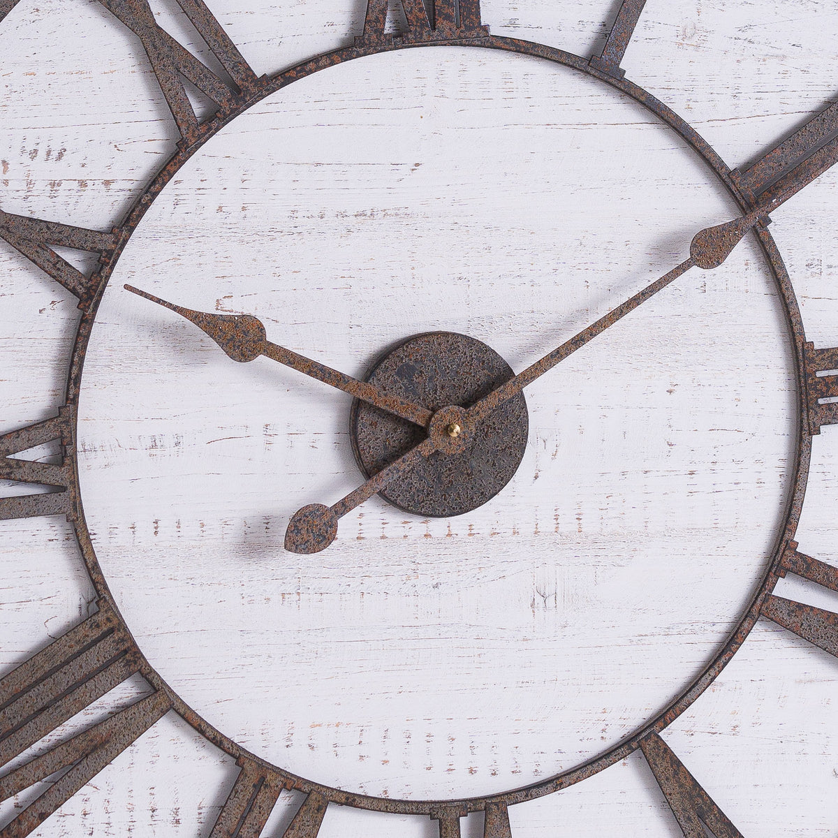 Close-up of the clock's mottled rust-brown hands and central disc against the distressed whitewashed face, with parts of the Roman numeral ring visible.
