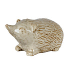 Cream-white hedgehog decoration facing left, with a raised pointed snout, short feet and a rounded back patterned with brown-shaded spines.