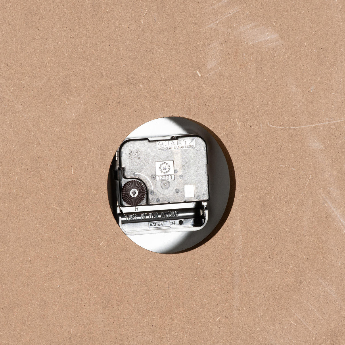 Rear close-up of the clock movement through a round cutout, with an empty battery compartment and visible AA 1.5V marking.