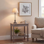 Table lamp on a grey side table beside books and a mug, with a framed branch print behind and a cream armchair alongside.