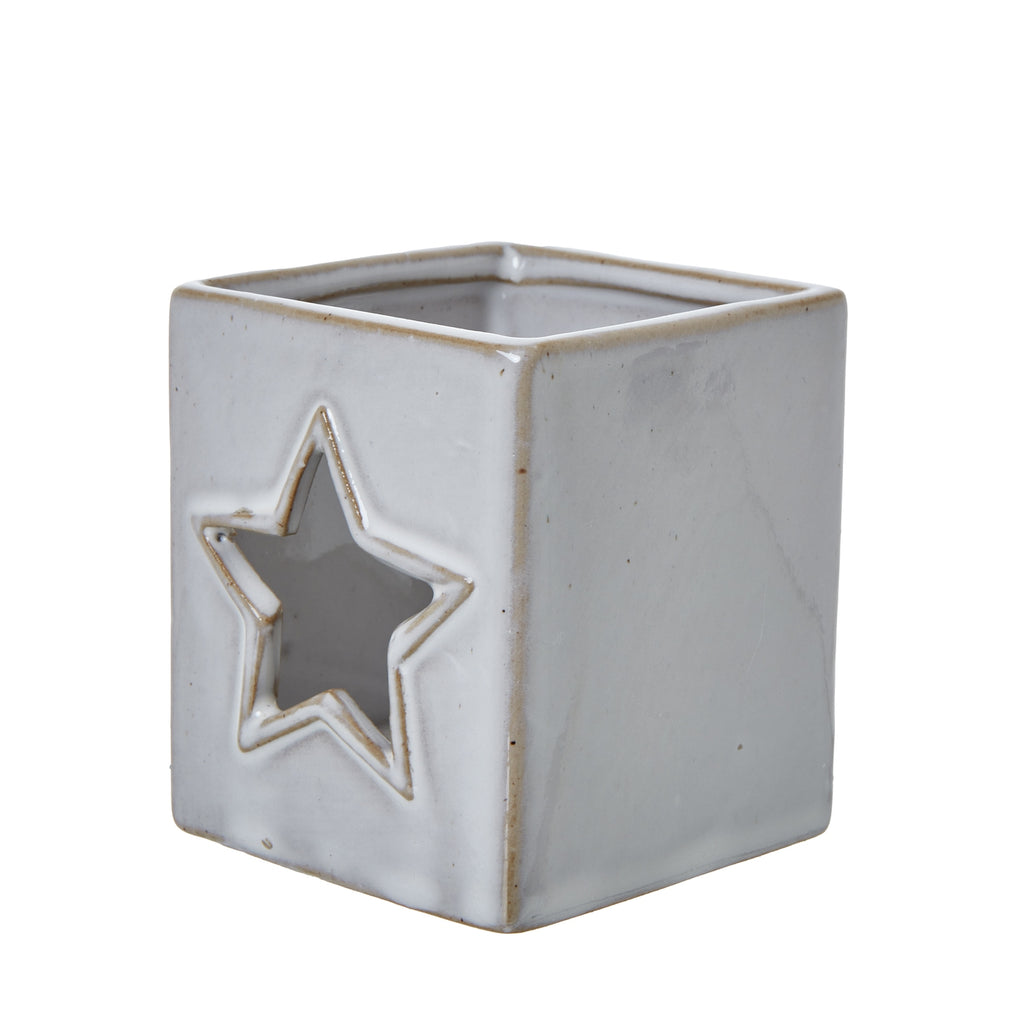 Angled view of the ceramic candle holder showing a star cut-out on one face, a plain side and the open square top.