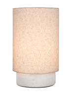 Table lamp switched on, showing a warm glow through its cream linen shade above the white marble base.