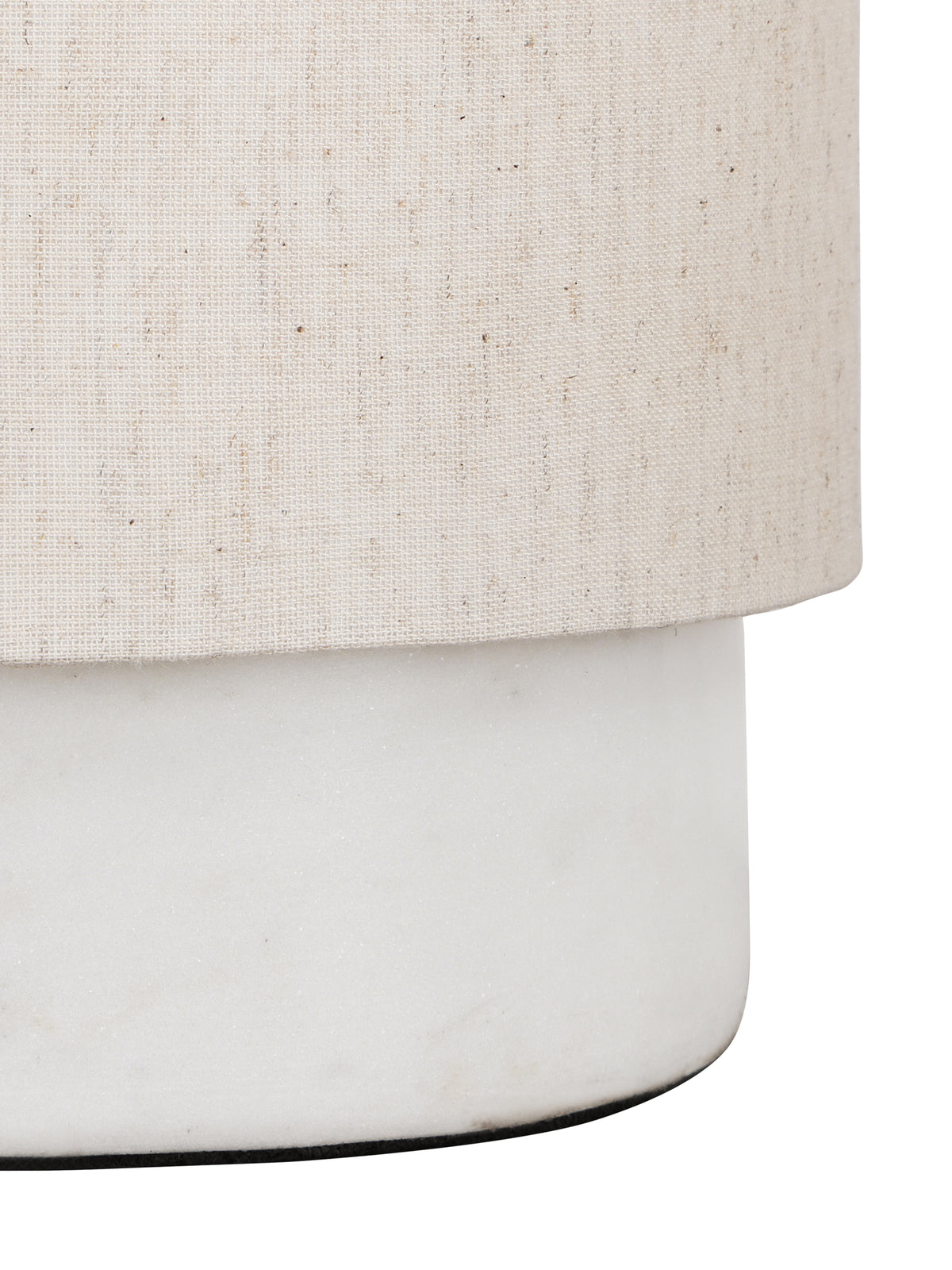 Angled close-up of the woven linen shade above the smooth white marble base and its rounded lower edge.