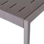 Close-up of the grey table corner, with staggered narrow slots, fine linear texture and a thick edge beside the square-section leg.